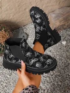 Detalle de botines Chelsea negros con estampado de mariposas blancas y suela track gruesa