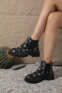 Vista detallada de botines Chelsea negros con estampado de mariposas y suela de plataforma.