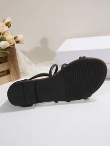 Detailed bottom view showing the non-slip wavy tread pattern of black flat sandal sole.