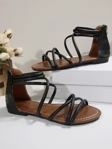 Detail of black flat gladiator sandals with crisscross straps and a back zipper.