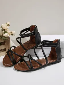 Black cross strap flat Roman sandals with back zipper and brown cushioned footbed detail.