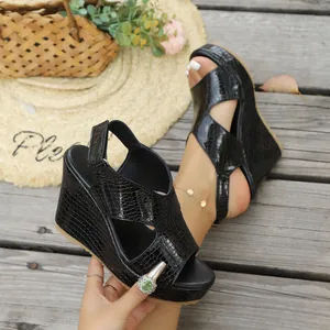 Detailopname van zwarte sleehak sandalen met krokodillenprint op een houten zomerterras