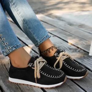 Close-up of women's black suede ethnic loafers with thick rope laces on wooden floor.