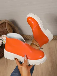 Detail showing bright orange ankle boot with thick white lug sole and back zipper