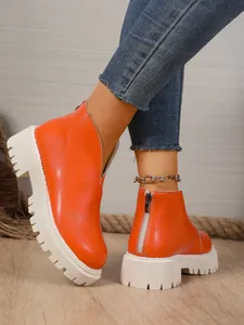 Detail side view of bright orange platform ankle boots with back zipper closure