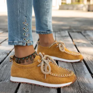 Detail view of women's yellow suede ethnic loafers with thick rope laces on wooden deck