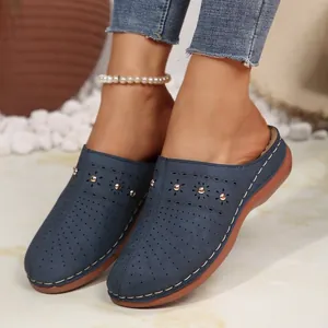 Dettaglio di sabot blu traforati con borchie metalliche e cuciture bianche a contrasto.