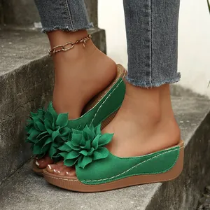 Primer plano de sandalias con cuña verdes con elegantes flores en 3D sobre escalones.