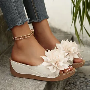 Elegantes sandalias de cuña beige con decoración floral 3D sobre escalones de piedra.