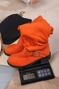 Vibrant orange slouchy suede boot being weighed on a digital scale weighing 571.3g