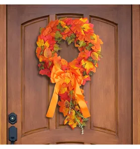 Detailed view of a vibrant autumn maple leaf wreath with orange bow hung on a wooden door