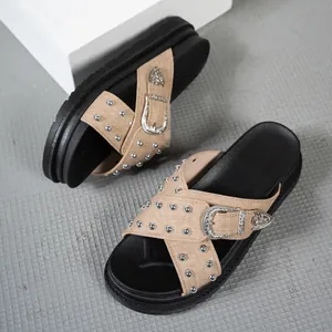 Primer plano de sandalias de plataforma beige con tachuelas y hebilla occidental.