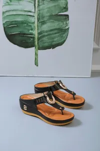 Detail view of black platform thong sandals featuring a B logo and metallic buckle.