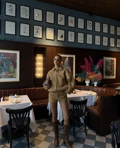 Elegantes Set aus beigefarbener Wildlederjacke und Shorts in einem Retro-Café-Ambiente