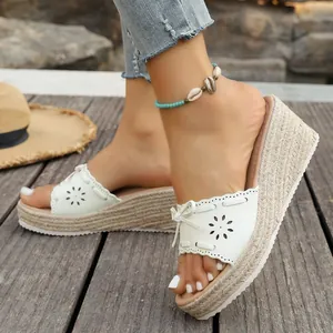 Dettaglio di sandali con zeppa bianchi con fiocco e motivi a fiori su ponte in legno