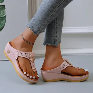 Close-up of pink wedge thong sandals with gold horseshoe buckle and hollow details.