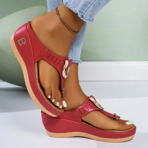Detailed view of red wedge thong sandals with metal B emblem and hollow laser-cut patterns