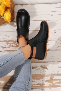 Detaillierte Ansicht schwarzer Lackleder-Stiefeletten mit flacher Sohle und blauer Jeans.