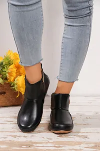Nahaufnahme von schwarzen flachen Stiefeletten Martin-Stil auf rustikalem Holzboden
