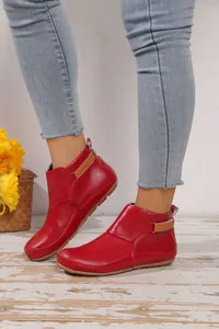 Detailansicht von roten flachen Lederstiefeletten mit Klettverschluss auf Holzboden