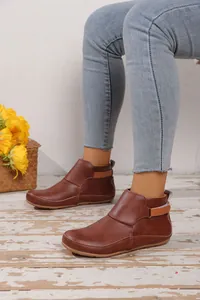 Detailansicht brauner Lederstiefeletten für Damen mit flacher Sohle auf einem rustikalen Boden