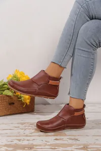 Detaillierte Nahaufnahme von braunen flachen Stiefeletten aus Kunstleder mit blauer Jeans