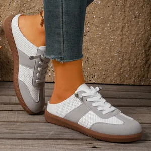 Close-up van witte en grijze geperforeerde mule sneakers op rustieke houten vloer