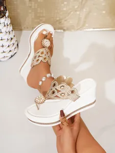 Macro view of white wedge thong sandals featuring rhinestones and pearl flower detail