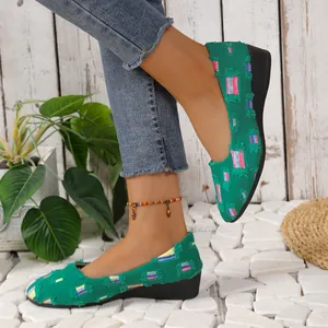 Primer plano de mocasines de cuña en tela verde con bordados coloridos y bordes deshilachados
