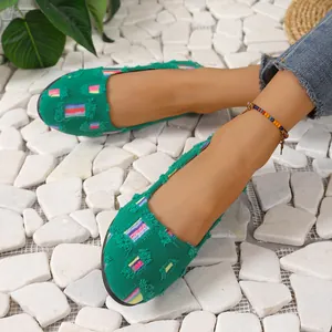 Primer plano de mocasines de lona verde con parches de rayas de colores y flecos.