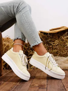 Vista detallada de zapatillas de lona crema con suela blanca gruesa sobre fondo rústico.