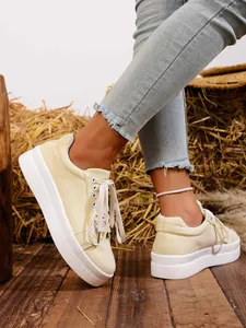 Vista detallada de zapatillas de lona amarillas con suela gruesa en suelo de madera rústica.