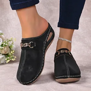 Close-up of black mules with gold chain detail and white contrast stitching
