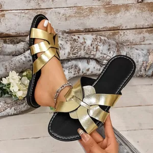 Detailansicht der goldmetallic-farbenen flachen Sandalen mit gekreuzten Riemen.