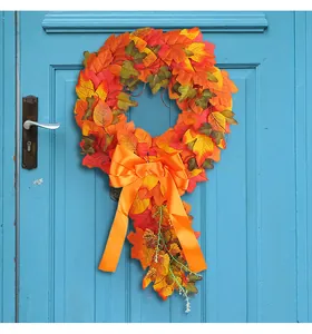 Artificial autumn harvest maple leaf wreath with large orange bow hanging on a blue door