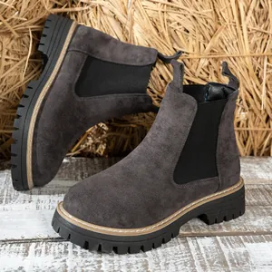 Primer plano de botas Chelsea de ante gris oscuro con suela gruesa en un entorno rústico