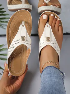 Nahaufnahme von weißen Keil-Flip-Flops mit Laserschnitt-Details und Goldschnalle