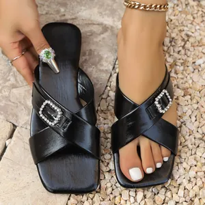 Detail view of black cross strap sandals with rhinestone buckles and square toe.