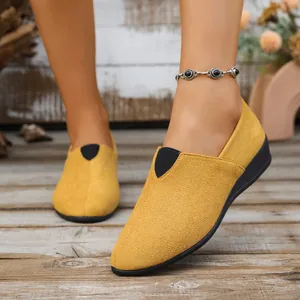 Close-up of yellow suede pointed-toe wedge loafers worn on a rustic wooden deck.