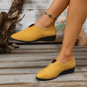 Close-up of yellow suede wedge slip-ons worn by a model in a rustic wooden environment