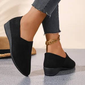 Detailed close-up of black suede pointed-toe wedge loafers worn with a gold chain anklet