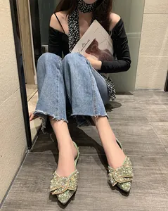 Elegante groene puntige platte schoenen met grote strass-strik op een model.
