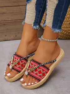 Nahaufnahme von roten böhmischen bestickten flachen Sandalen mit metallischen Details.