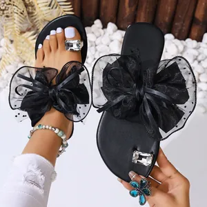 Détail de sandales plates d'été noires avec un grand nœud en mesh et un anneau en strass.