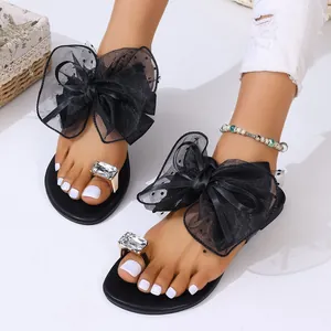 Détail de sandales plates noires avec gros nœud en résille et boucle d'orteil en strass