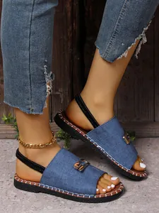 Vue détaillée de sandales plates en denim bleu avec boucle dorée et bride élastique au pied.