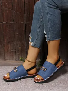 Gros plan de sandales plates en denim bleu avec boucle dorée et bride élastique.