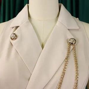 Close-up view of beige notched lapel blazer jumpsuit with gold buttons and chain details