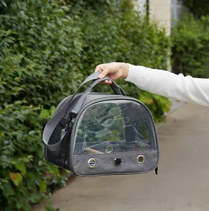 Portable grey bird carrier bag with transparent window and mesh vents held outdoors.