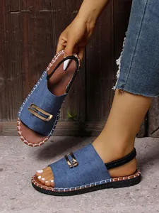 Gros plan sur les sandales plates en jean bleu avec boucle dorée et bride élastique